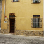 "Façana de dos pisos amb porta de fusta i finestra amb reixes, estil rustic."