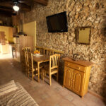 "Menjador amb taula de fusta, cadires i televisor muntat a la paret de pedra."