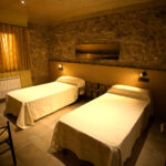 "Dormitori amb dos llits individuals, parets de pedra i llum tènue."